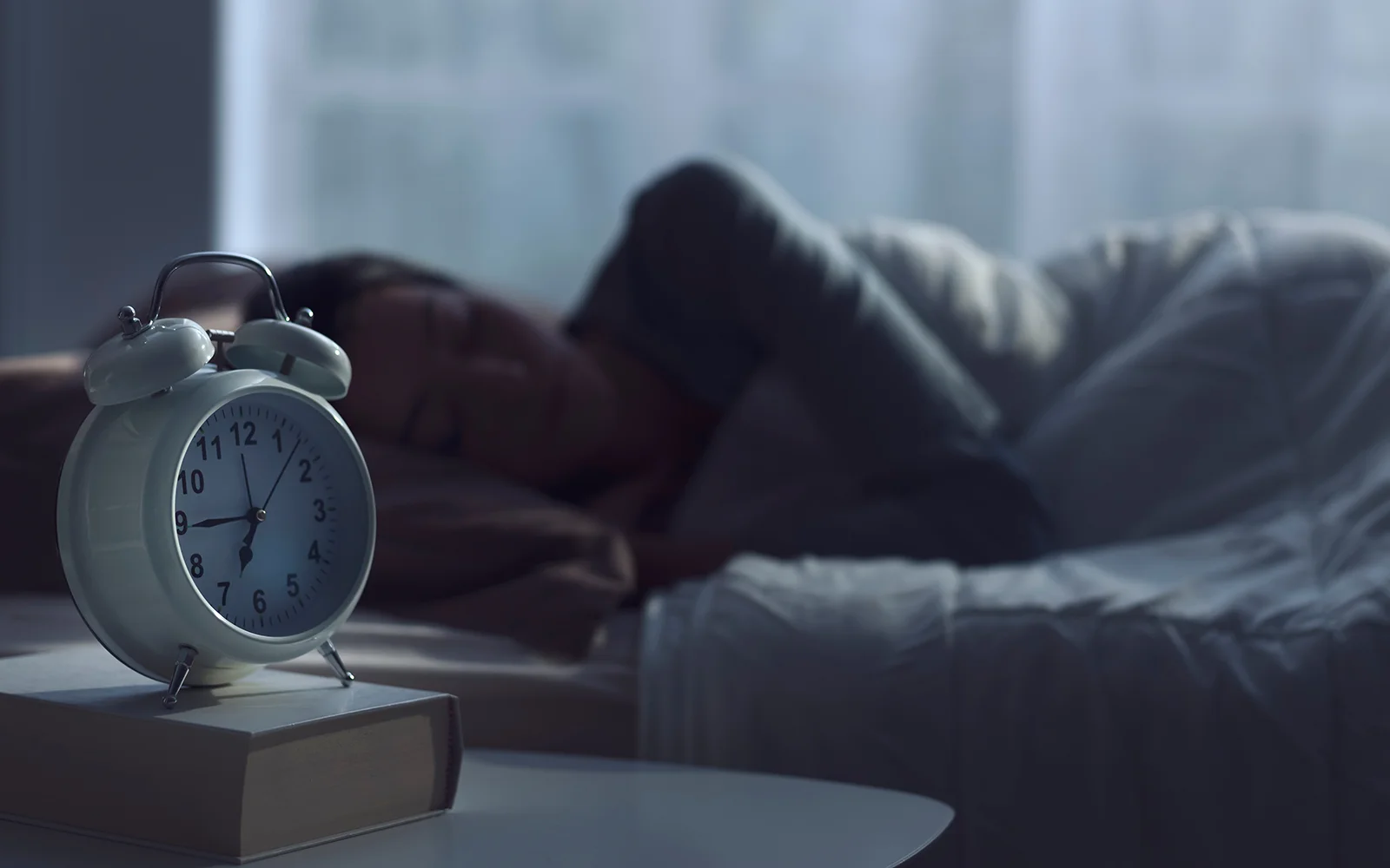 Woman awake in bed at night looking at a bedside clock